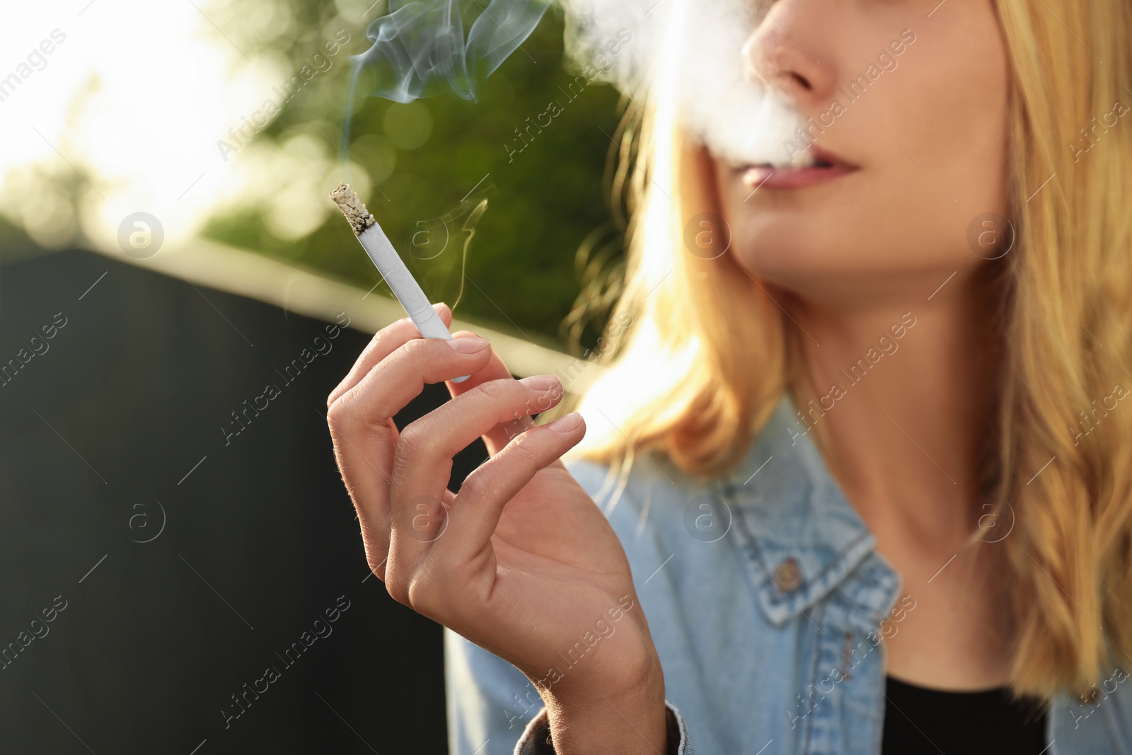 Photo of Young woman smoking cigarette outdoors, closeup view