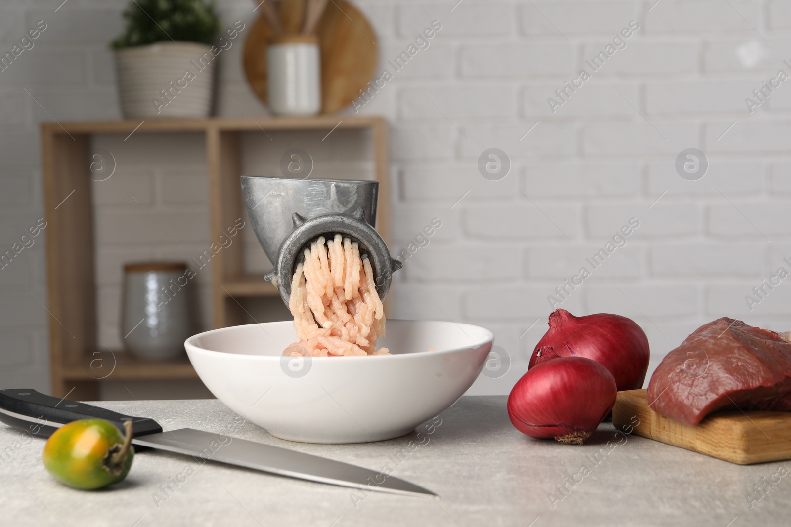 Photo of Metal meat grinder with chicken mince and products on light grey table indoors