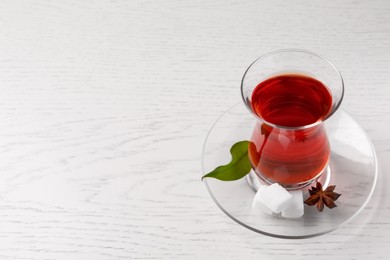 Photo of Glass of traditional Turkish tea and sugar cubes on white wooden table. Space for text