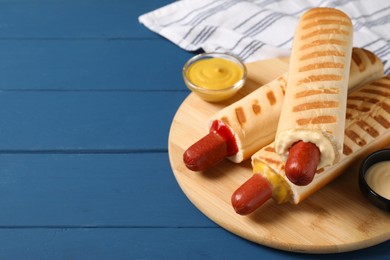 Tasty french hot dogs with different sauces on blue wooden table, space for text