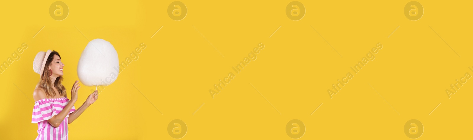 Image of Young woman with sweet cotton candy on yellow background, space for text. Banner design