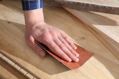 Photo of Man polishing wooden planks with sandpaper, closeup
