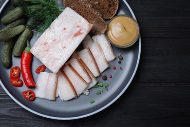 pork fatback with spices, rye bread and pickled cucumbers on black wooden table, top view