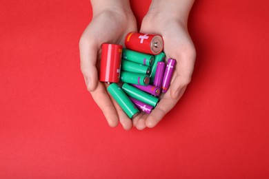 Photo of Woman holding many different batteries on red background, top view