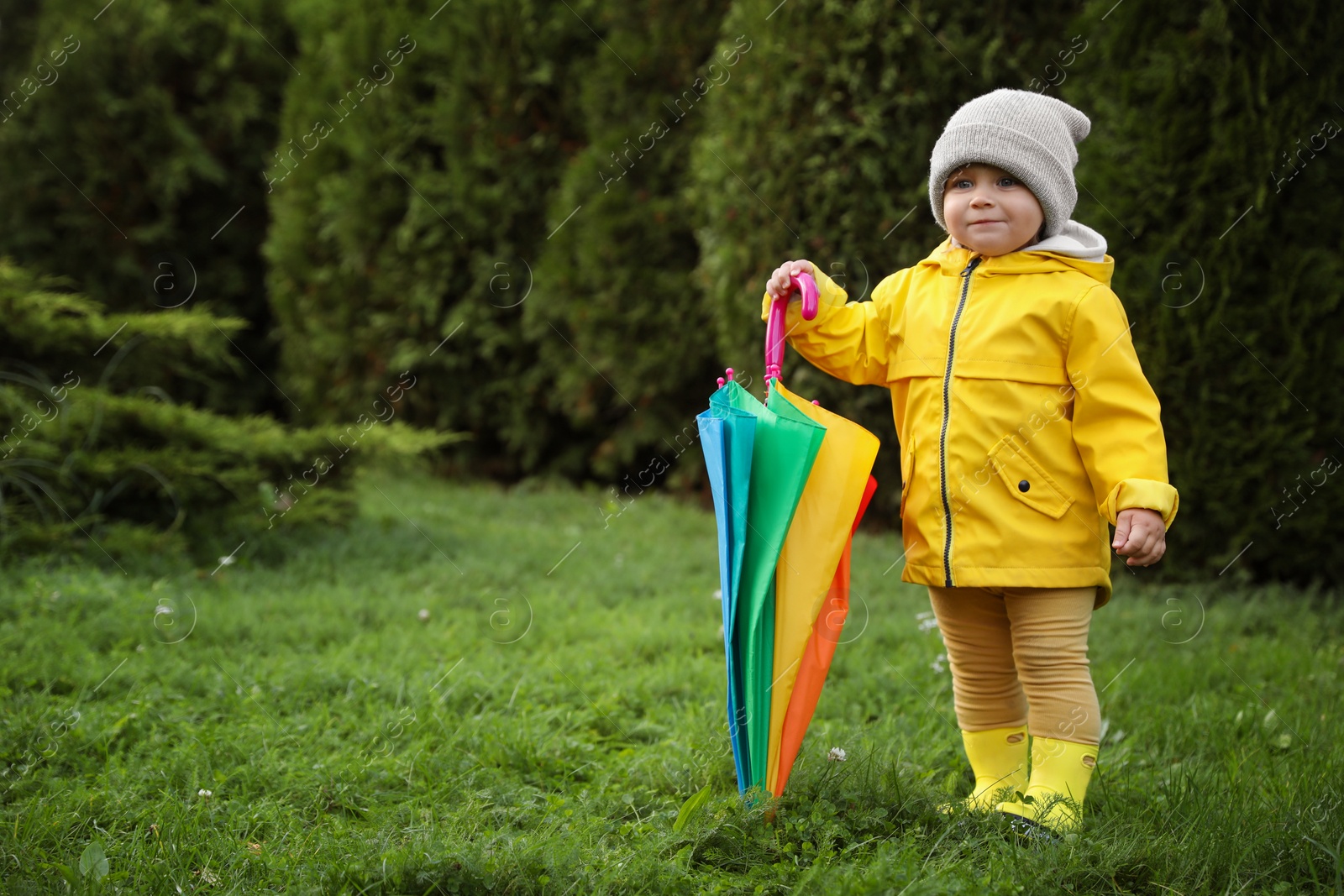 Photo of Cute little girl holding colorful umbrella in garden, space for text