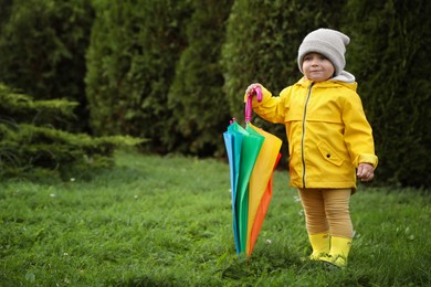 Photo of Cute little girl holding colorful umbrella in garden, space for text