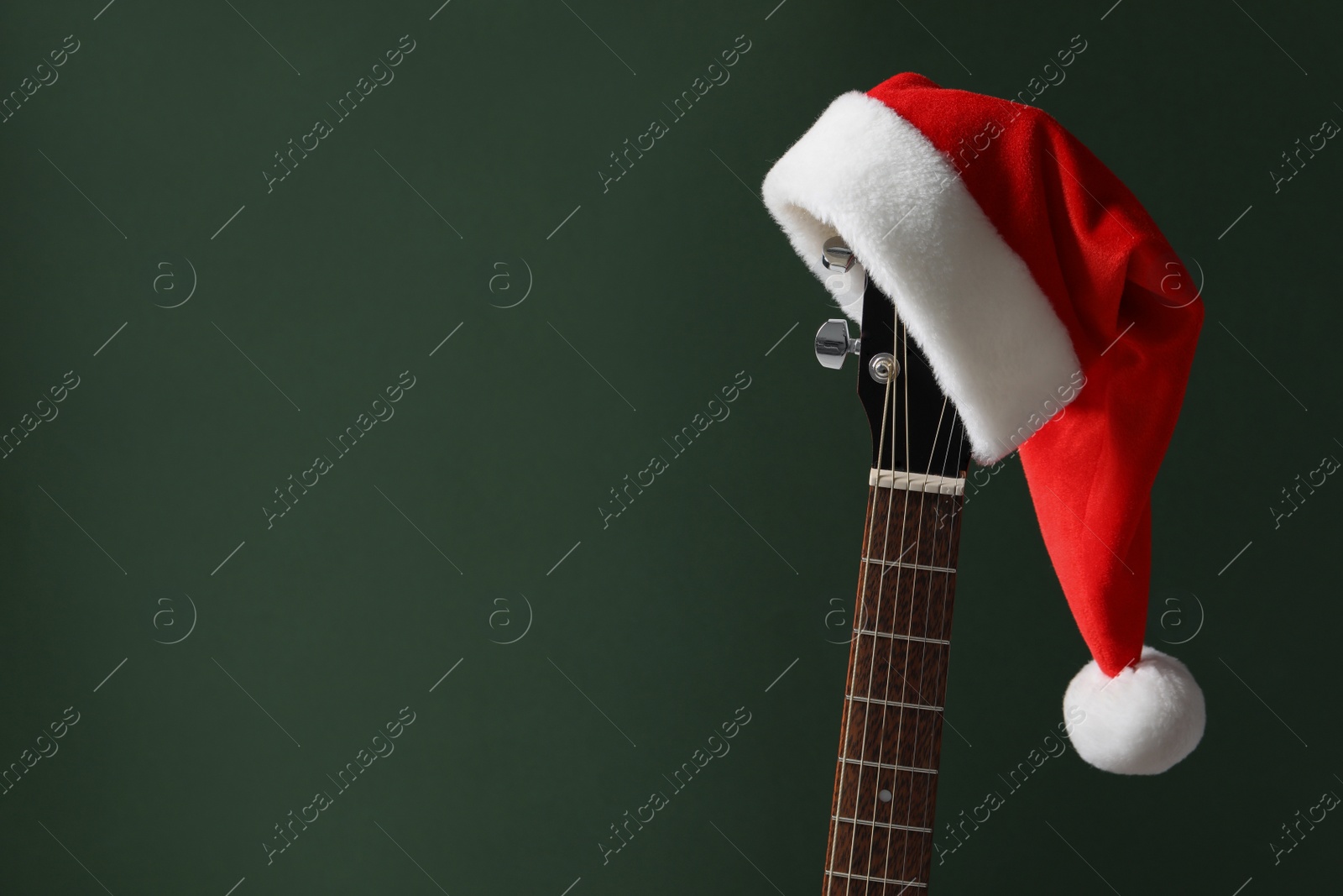 Photo of Guitar with Santa hat on green background, space for text