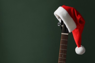 Photo of Guitar with Santa hat on green background, space for text