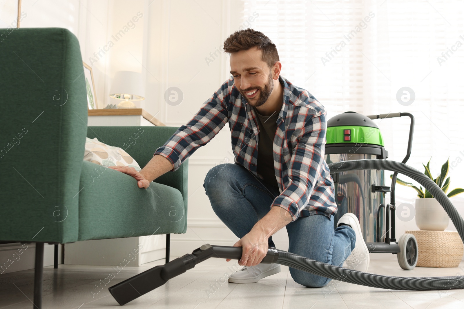 Photo of Man vacuuming floor under sofa in living room