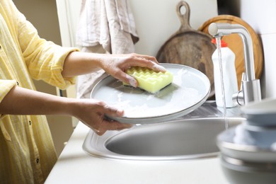 Woman washing plate in kitchen sink, closeup