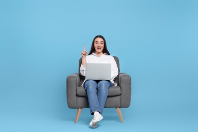 Photo of Happy young woman with laptop sitting in armchair on light blue background