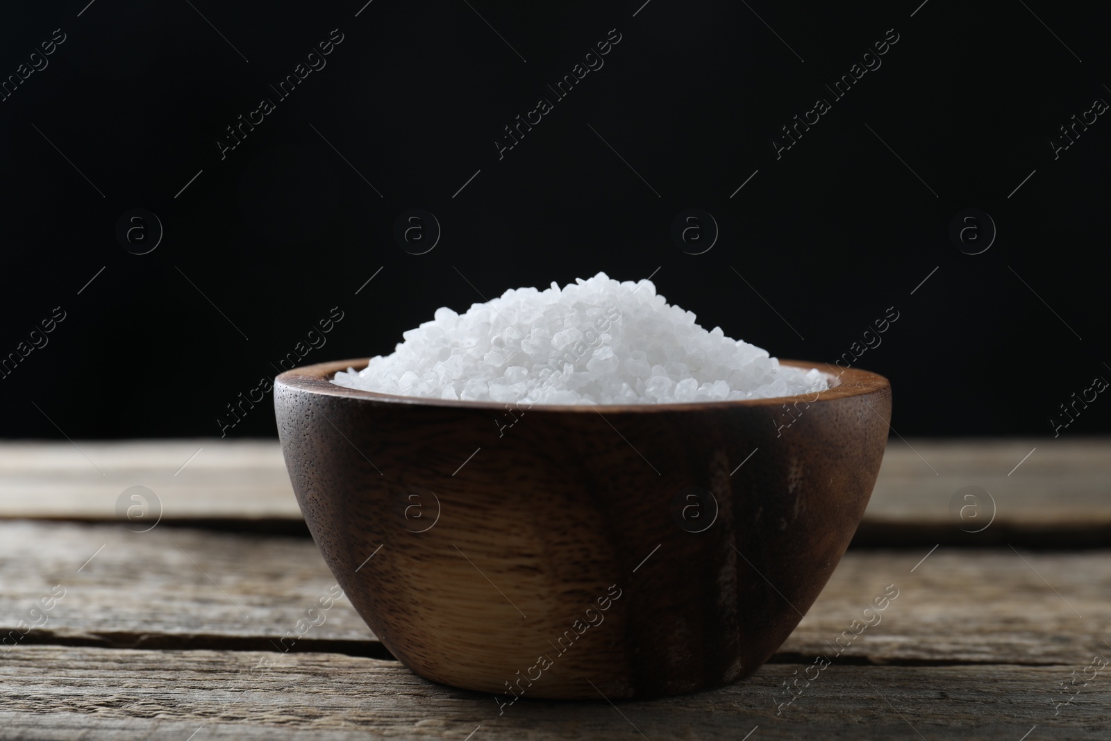 Photo of Organic salt in bowl on wooden table, closeup