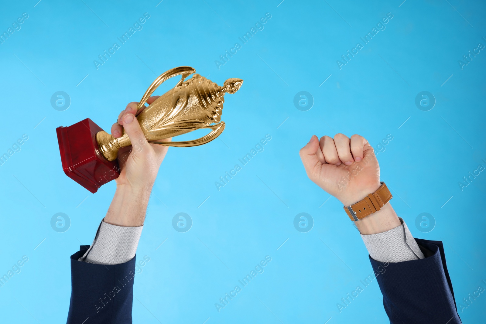 Photo of Businessman holding gold trophy cup on light blue background, closeup