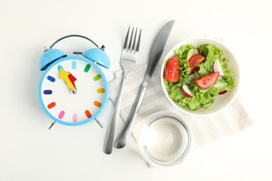 Photo of Alarm clock and salad on white background, top view. Meal timing concept