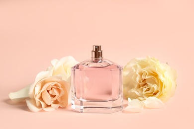 Photo of Bottle of perfume and beautiful flowers on beige background