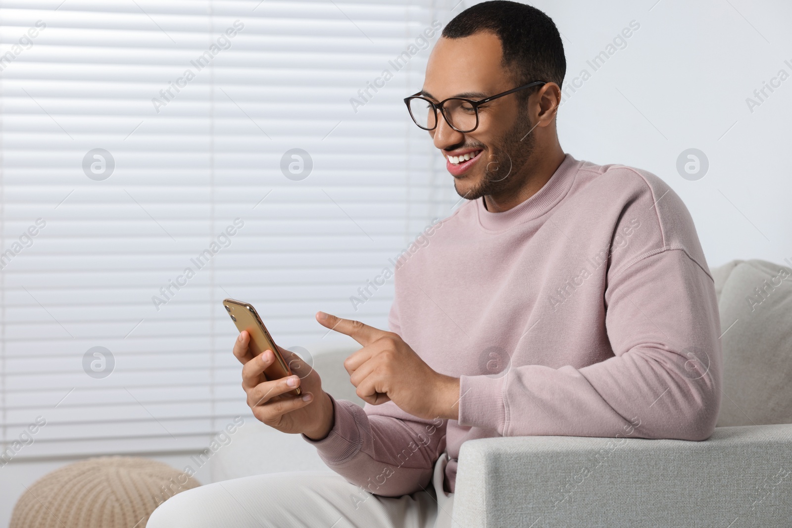 Photo of Happy man sending message via smartphone at home