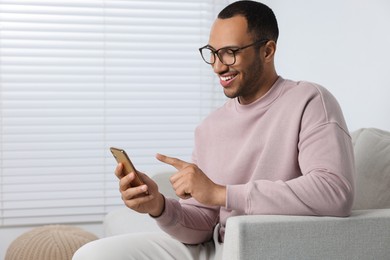 Photo of Happy man sending message via smartphone at home