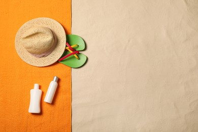 Photo of Beach towel, hat, sun protection products and flip flops on sand, flat lay. Space for text