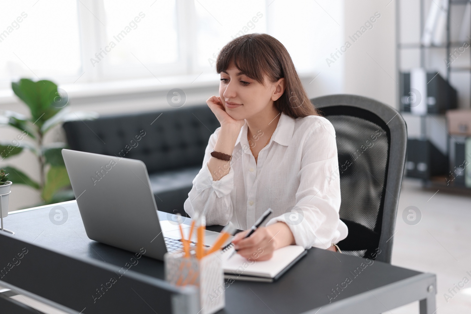 Photo of Woman taking notes during webinar at table indoors