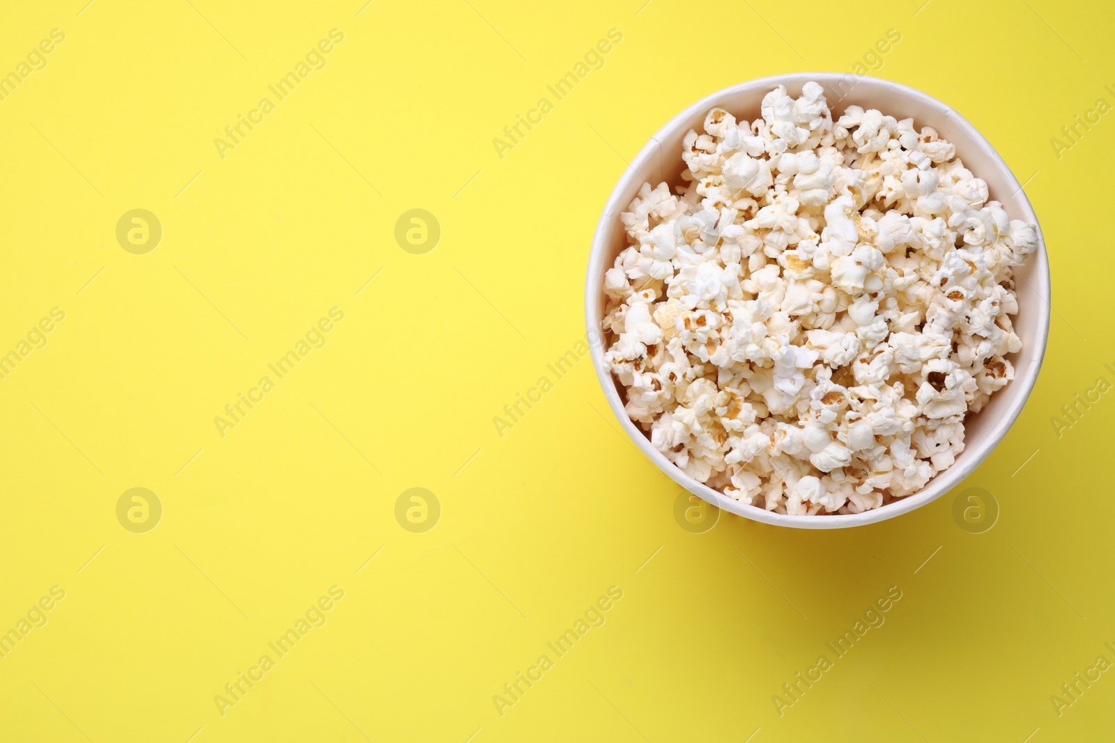 Photo of Paper bucket with delicious popcorn on yellow background, top view. Space for text