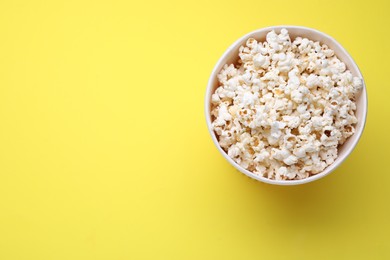 Photo of Paper bucket with delicious popcorn on yellow background, top view. Space for text