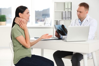 Photo of Doctor with neck MRI image consulting patient in clinic