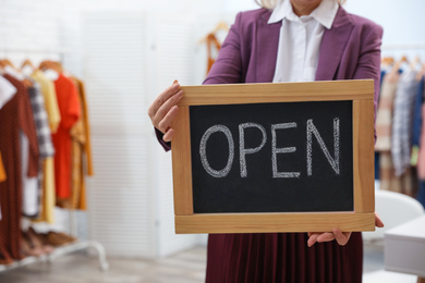 Female business owner holding OPEN sign in boutique, closeup