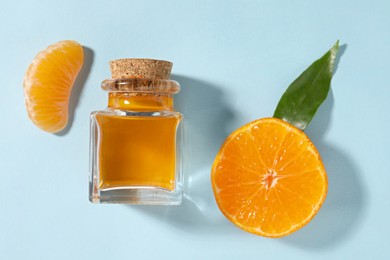 Aromatic tangerine essential oil in bottle and citrus fruit on light blue table, top view