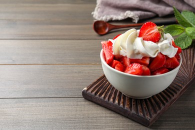 Photo of Delicious strawberries with whipped cream served on wooden table. Space for text