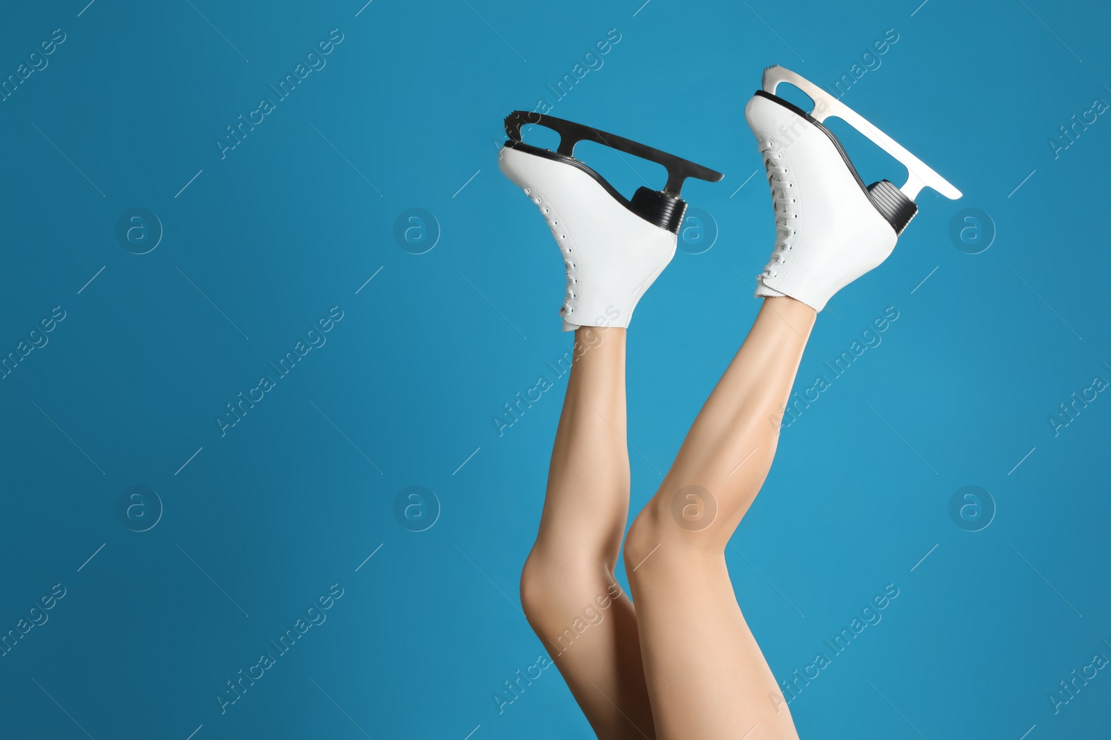 Photo of Woman in elegant white ice skates on light blue background, closeup of legs. Space for text