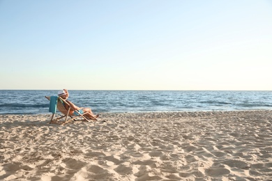 Young man relaxing in deck chair on beach near sea