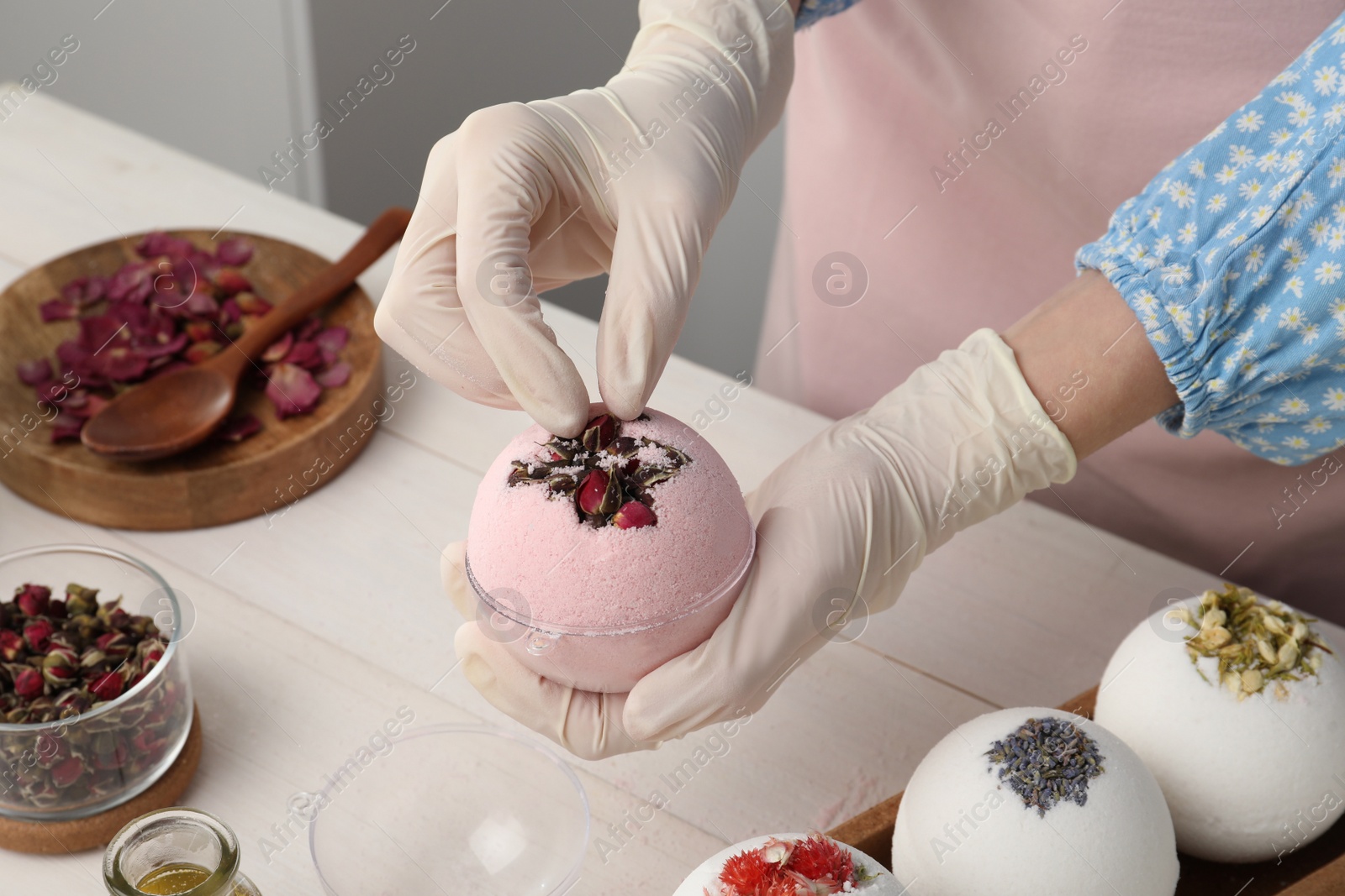 Photo of Woman in gloves making bath bomb at white table, closeup