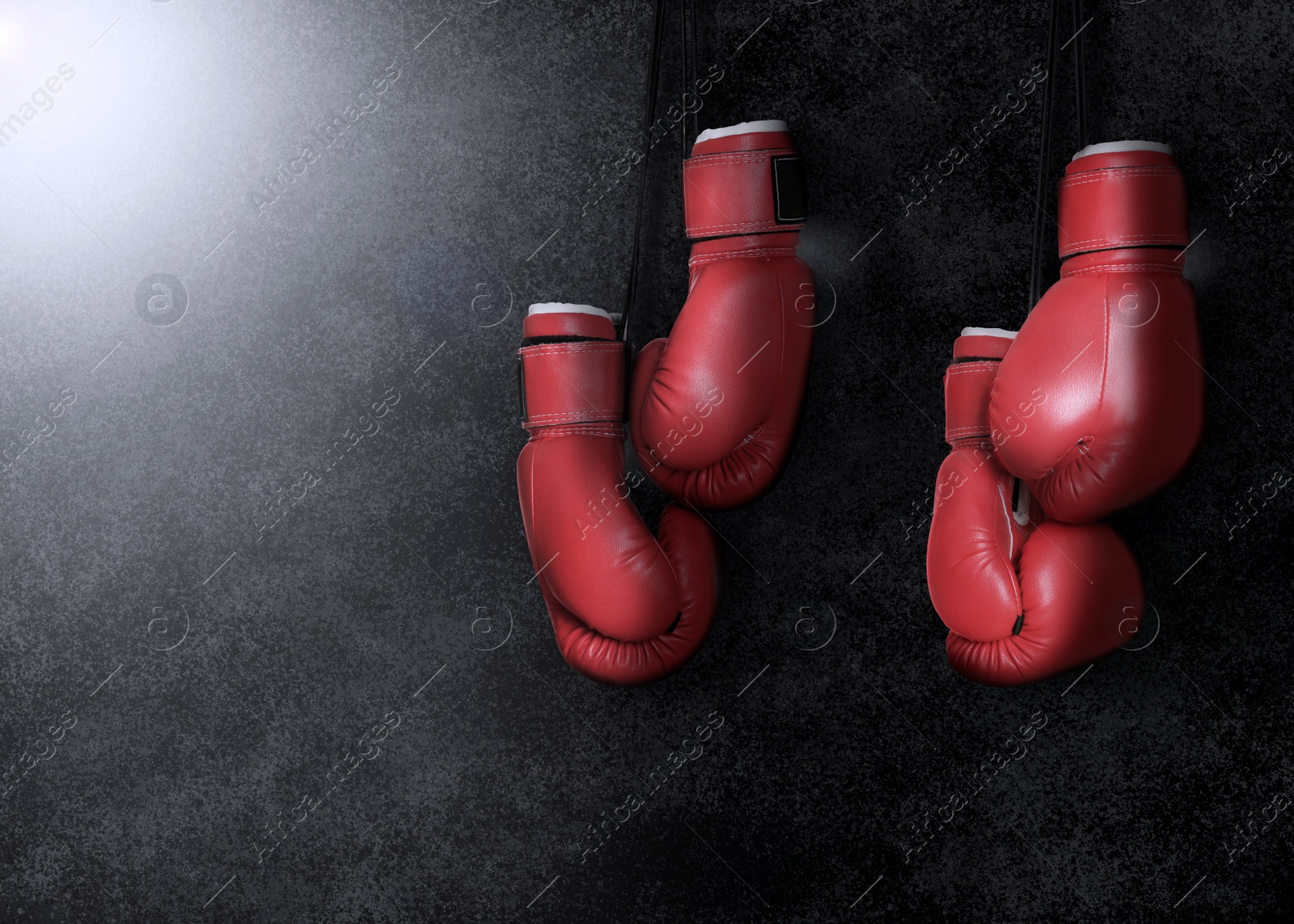 Image of Two pairs of boxing gloves hanging against dark background