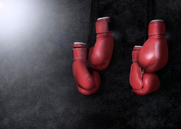 Image of Two pairs of boxing gloves hanging against dark background