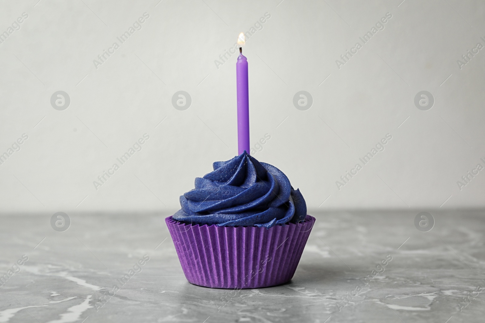 Photo of Delicious birthday cupcake with cream and burning candle on marble table