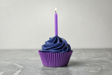 Delicious birthday cupcake with cream and burning candle on marble table