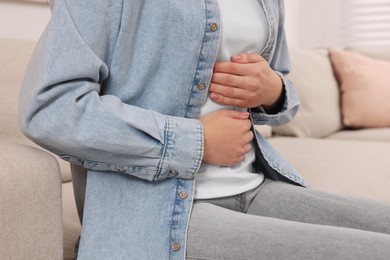 Photo of Young woman suffering from stomach pain on sofa indoors, closeup