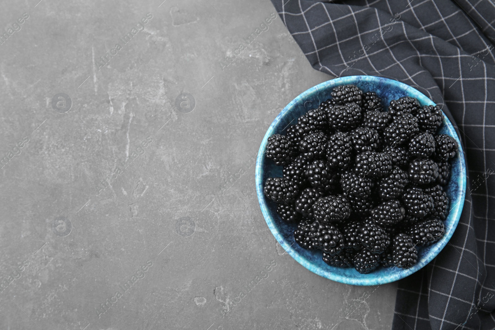 Photo of Bowl of ripe blackberries on grey table, flat lay. Space for text