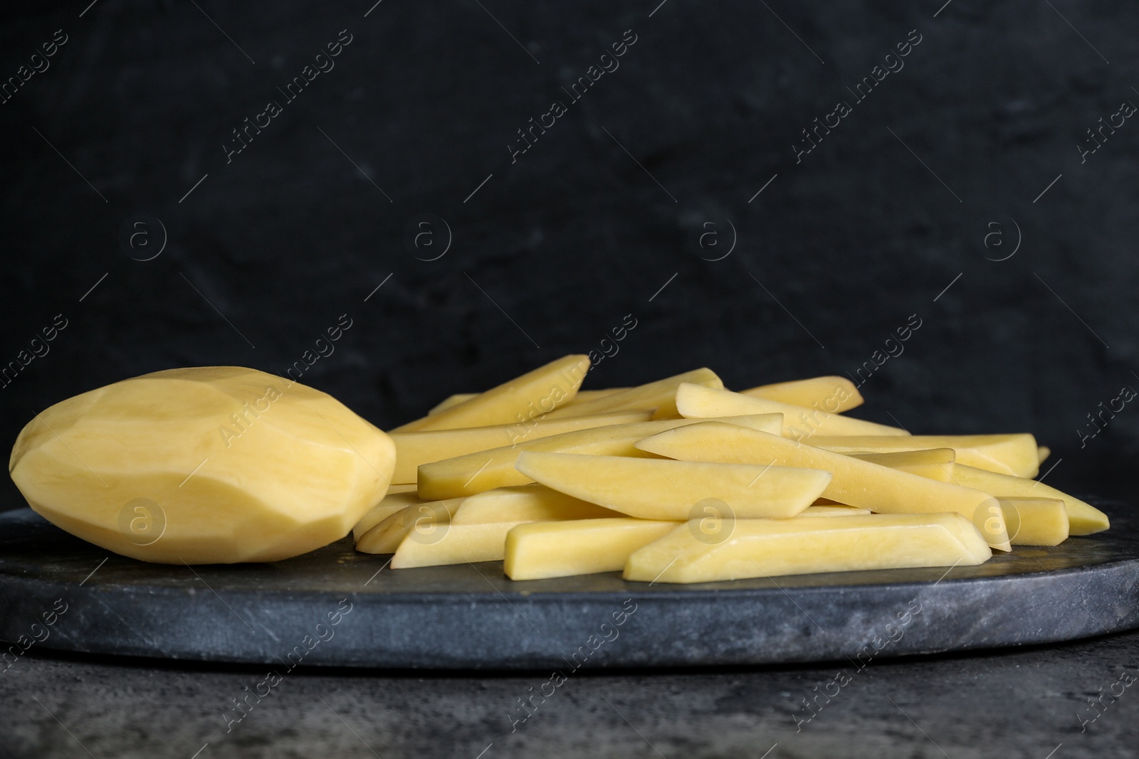 Photo of Whole and cut raw potatoes on grey table, closeup. Cooking delicious French fries