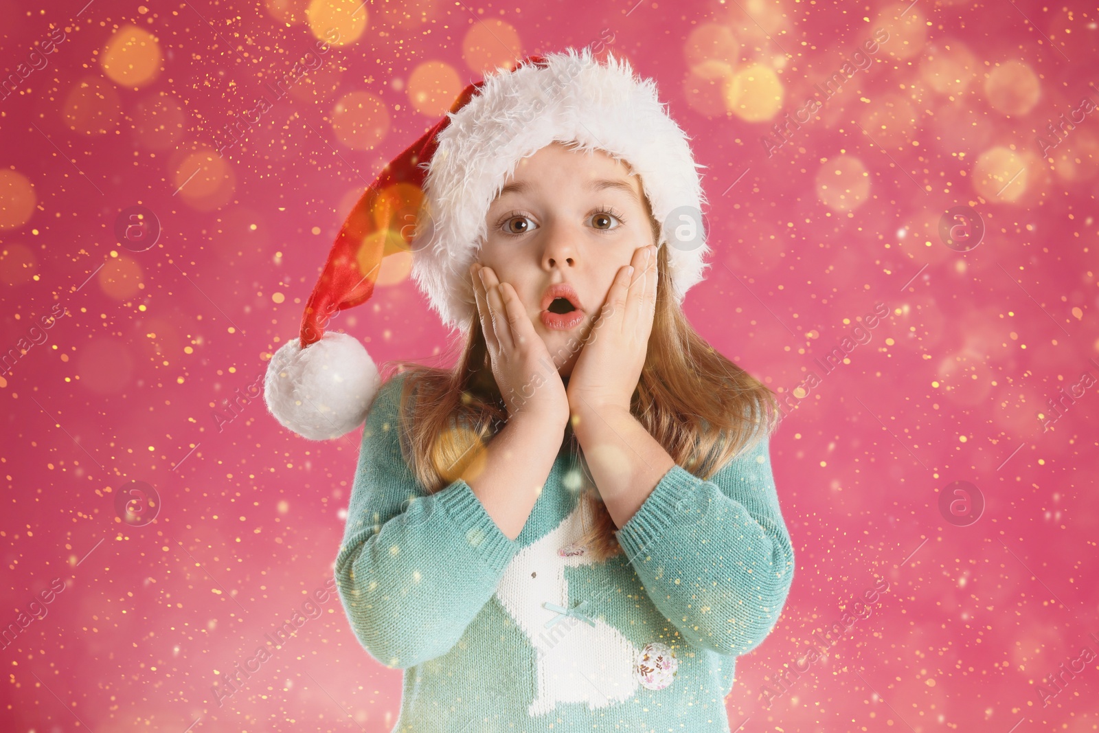 Image of Cute child in Santa hat on pink background. Christmas celebration