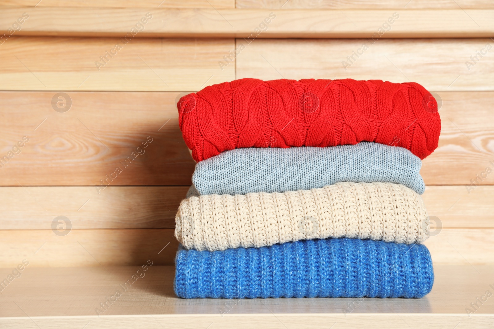 Photo of Stack of winter clothes against wooden background. Space for text