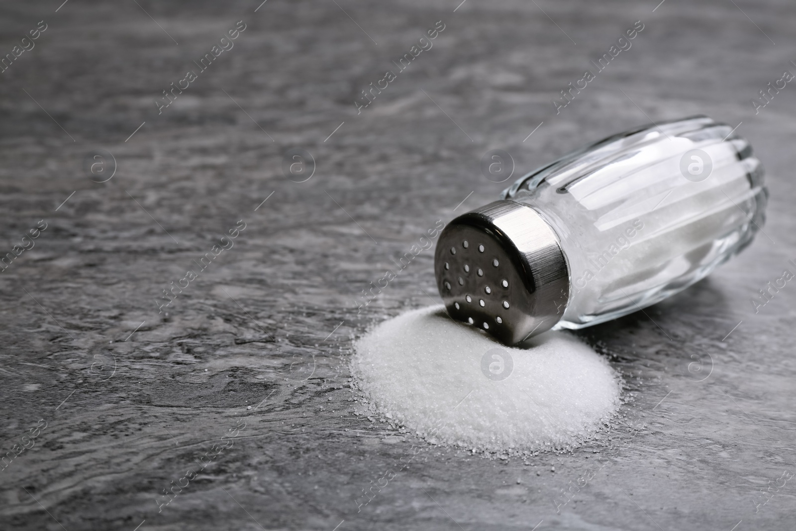 Photo of Scattered salt and shaker on grey table, closeup. Space for text