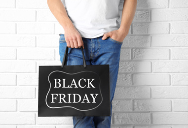 Man holding shopping bag with text BLACK FRIDAY against brick wall, closeup