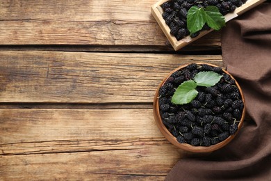 Bowl and box with ripe black mulberries on wooden table, flat lay. Space for text