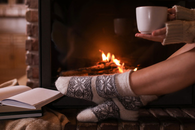 Photo of Woman with cup of hot cocoa near fireplace indoors, closeup