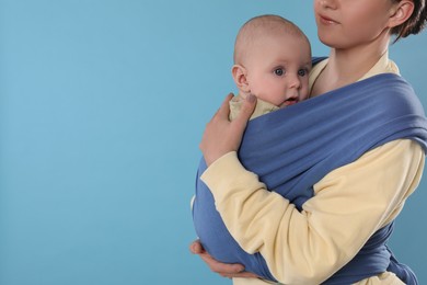 Photo of Mother holding her child in sling (baby carrier) on light blue background, closeup. Space for text