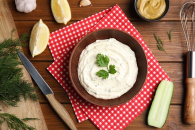 Photo of Delicious tartar sauce and ingredients on wooden table, flat lay