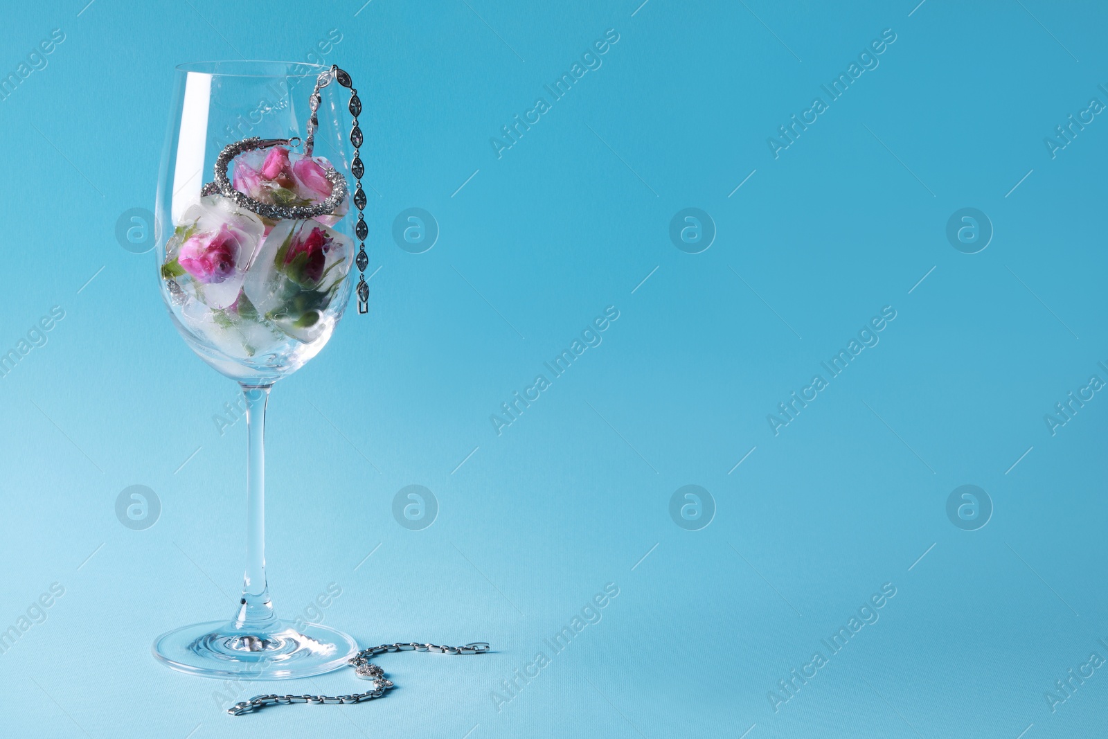 Photo of Elegant jewelry. Stylish presentation with luxury earrings, bracelets and frozen roses in glass on light blue background. Space for text