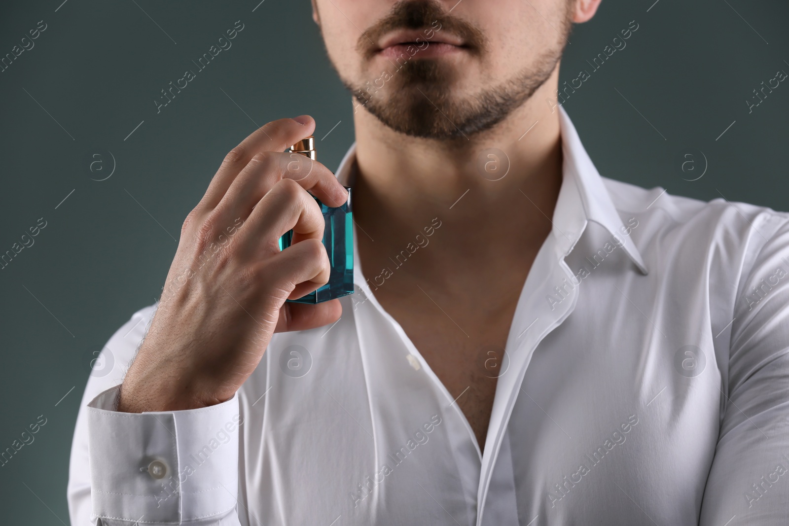 Photo of Handsome man in shirt using perfume on dark background, closeup