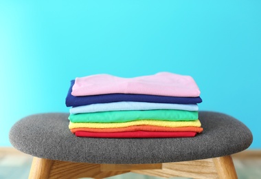 Photo of Stack of rainbow clothes on stool against color background